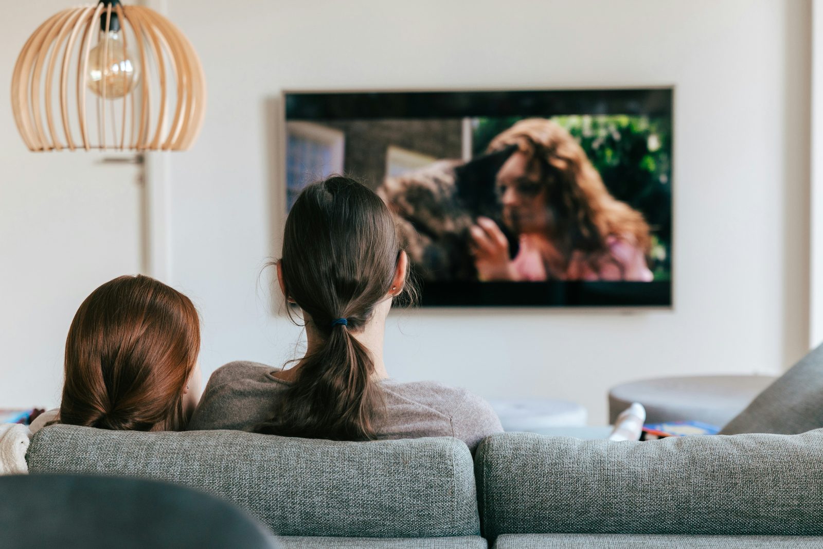 Two people relaxing together on a sofa at home, watching television in warm evening light.