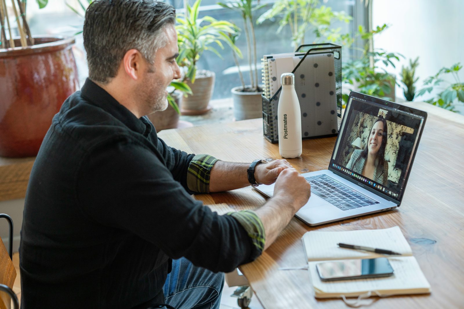 A person working from home on a laptop video call at a sunlit desk.